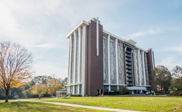 Charlotte apartment for rent - A large, modern building with a red and white facade stands in a grassy area with trees in the background.