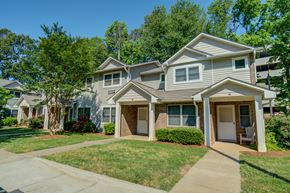 Charlotte apartment for rent - A house with a grey roof and a white door is surrounded by greenery.