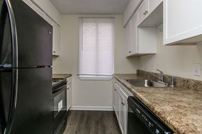 Atlanta apartment for rent - A black refrigerator sits in a kitchen with white cabinets and a granite countertop.