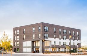 Aurora apartment for rent - Northeast exterior view of Peoria Crossing, main entrance doors on north east corner, top half grey brick, bottom half white siding on east side of building
