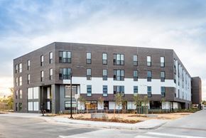 Aurora apartment for rent - Exterior shot of Peoria Crossing Apartments, grey bricks on top half, windows, and white siding on lower half