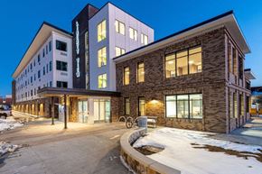 Aurora apartment for rent - A modern building with a mix of stone and glass facades is illuminated at dusk.