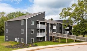 Grand Rapids apartment for rent - A grey apartment building with a balcony and a small garden in front.
