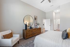 Orlando apartment for rent - A bedroom with a large bed, a white chair, and a wooden dresser with a mirror above it.