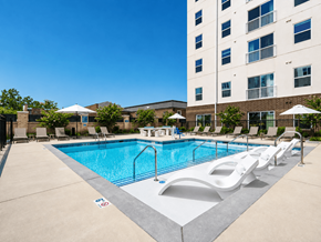Kannapolis apartment for rent - A large swimming pool with lounge chairs and umbrellas in front of a tall building.