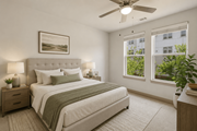 Herndon apartment for rent - A bedroom with a large bed, a ceiling fan, and a window with a view of a building and trees outside.