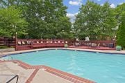 Woodbridge apartment for rent - A large outdoor swimming pool surrounded by trees and a red fence.