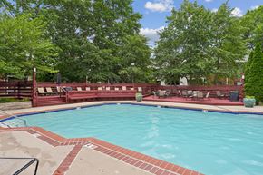 Woodbridge apartment for rent - A large outdoor swimming pool surrounded by trees and a red fence.