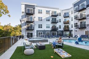 Minnetrista apartment for rent - two people sitting in lawn chairs near a swimming pool in front of an apartment building
