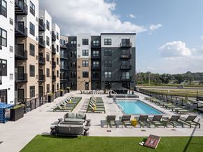 Minnetonka apartment for rent - A large outdoor pool area with sun loungers and a hot tub in front of a modern apartment block.