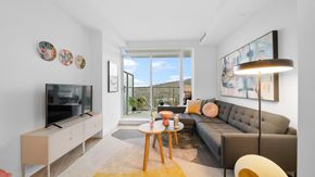 Coquitlam apartment for rent - A living room with a grey couch, a wooden table, a television, and a large window.