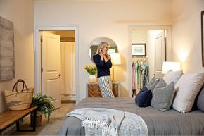 Mount Pleasant apartment for rent - A woman is standing in a bedroom with a bed, a mirror, and a potted plant.