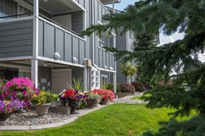 Spokane apartment for rent - A grey building with a balcony and a garden in front of Morning Glory Circle Apartments, 99208