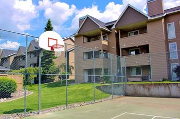 A basketball hoop is mounted on a chain link fence in front of apartment buildings.