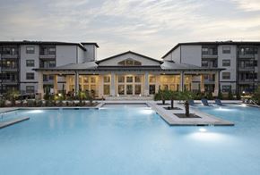 Fort Worth apartment for rent - A large swimming pool in front of a building with a spacious deck and lounge chairs.