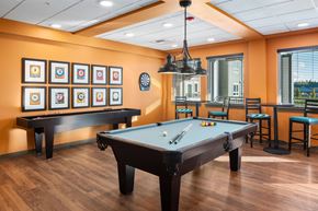 Arlington apartment for rent - A pool table is in the middle of a room with a bar and framed pictures on the wall.