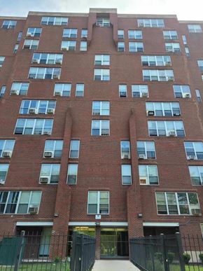 Chicago apartment for rent - A tall red brick building with many windows and a black fence in front.