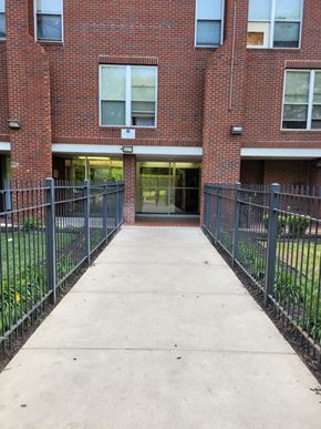 Chicago apartment for rent - A brick building with a black fence and a concrete walkway.