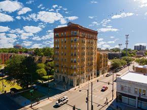 Chicago apartment for rent - A large yellow building is in the middle of a street with cars and traffic lights.