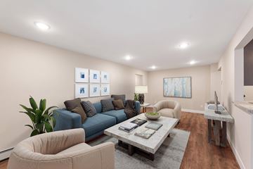 Chanhassen apartment for rent - A living room with a blue couch, a grey coffee table, a beige armchair, and a painting on the wall.