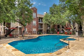San Antonio apartment for rent - A swimming pool surrounded by trees and a building in the background.