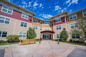 Oakdale apartment for rent - A building with a red and beige facade has a wooden bench in front of it.