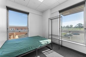Painesville apartment for rent - A bedroom with a bed, a window with a view of a building and trees, and a hanging clothes rack.
