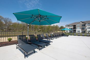 A row of lounge chairs under an umbrella on a white patio