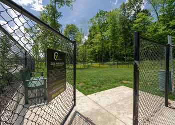 The gate to the dog park is open and there is a green lawn and trees