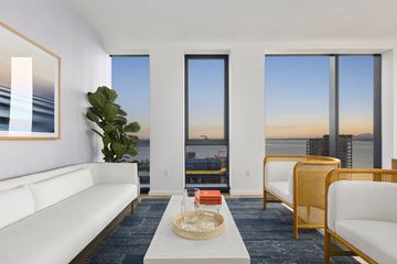 Seattle apartment for rent - A living room with a white sofa, a wooden chair, and a coffee table in front of a window with a view of the city.