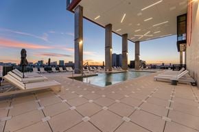 Houston apartment for rent - A rooftop pool area with sun loungers and a view of the city skyline at sunset.