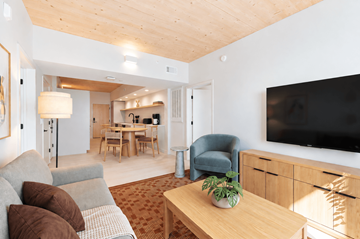 Charlotte apartment for rent - A living room with a grey couch, a wooden coffee table, a blue armchair, a wooden dining table with chairs, a flat screen TV, and a wooden ceiling.