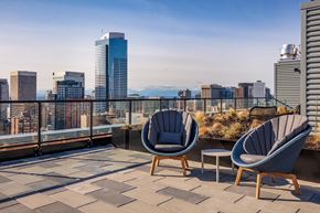 Seattle apartment for rent - Two chairs and a table are on a balcony with a city skyline in the background.
