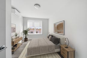 Norwalk apartment for rent - A bedroom with a bed, nightstand, and a window overlooking a cityscape.