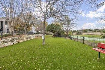 A grassy area with a bench and trees in front of a house