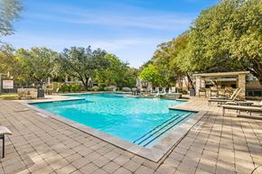 Austin apartment for rent - A large outdoor swimming pool surrounded by trees and a patio area with sun loungers.