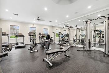 A gym with cardio equipment and weights in a building with windows