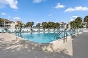 Indialantic apartment for rent - A large outdoor swimming pool surrounded by palm trees and lounge chairs.