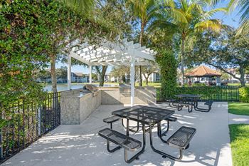 A white pergola is situated over a table and chairs in a park.