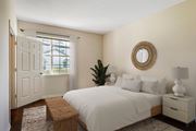 Fort Myers apartment for rent - A bedroom with a white bed, a wooden bench, and a round mirror on the wall.