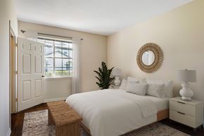 Fort Myers apartment for rent - A bedroom with a white bed, a wooden bench, and a round mirror on the wall.