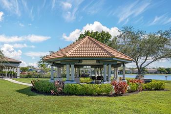 A gazebo with a red roof is surrounded by greenery and flowers.
