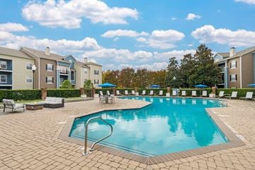 Charlotte apartment for rent - A large swimming pool surrounded by a brick patio and lounge chairs.