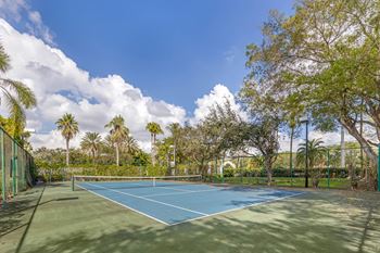 A tennis court surrounded by green fencing and trees.