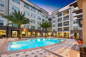 Orlando apartment for rent - a pool area with palm trees and a building in the background at The Rialto, Orlando, FL, 32819