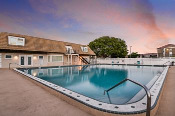 A large swimming pool in front of a building with a sunset in the background