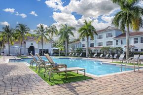 Jupiter apartment for rent - A pool surrounded by palm trees and lounge chairs.
