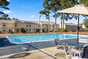 Wilmington apartment for rent - A pool area with chairs and an umbrella in front of apartment buildings.