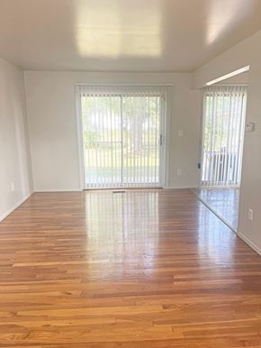 Inkster apartment for rent - A bright living room with a sliding glass door that leads to the outdoors. The floors are shining wood and the walls are light colored.