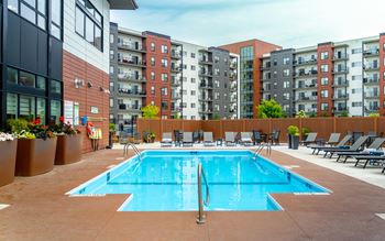 A large swimming pool surrounded by lounge chairs and apartment buildings.